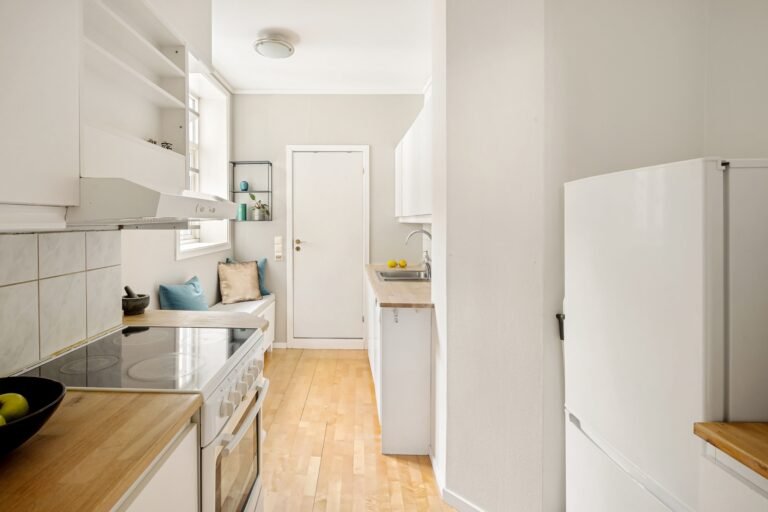 Modern white kitchen with wooden floors and minimalistic design, featuring a cozy seating area.